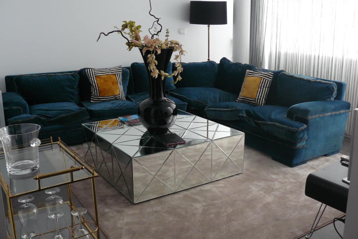 Uma sala de estar com um sofá azul, uma mesa de centro de vidro e um vaso com flores.