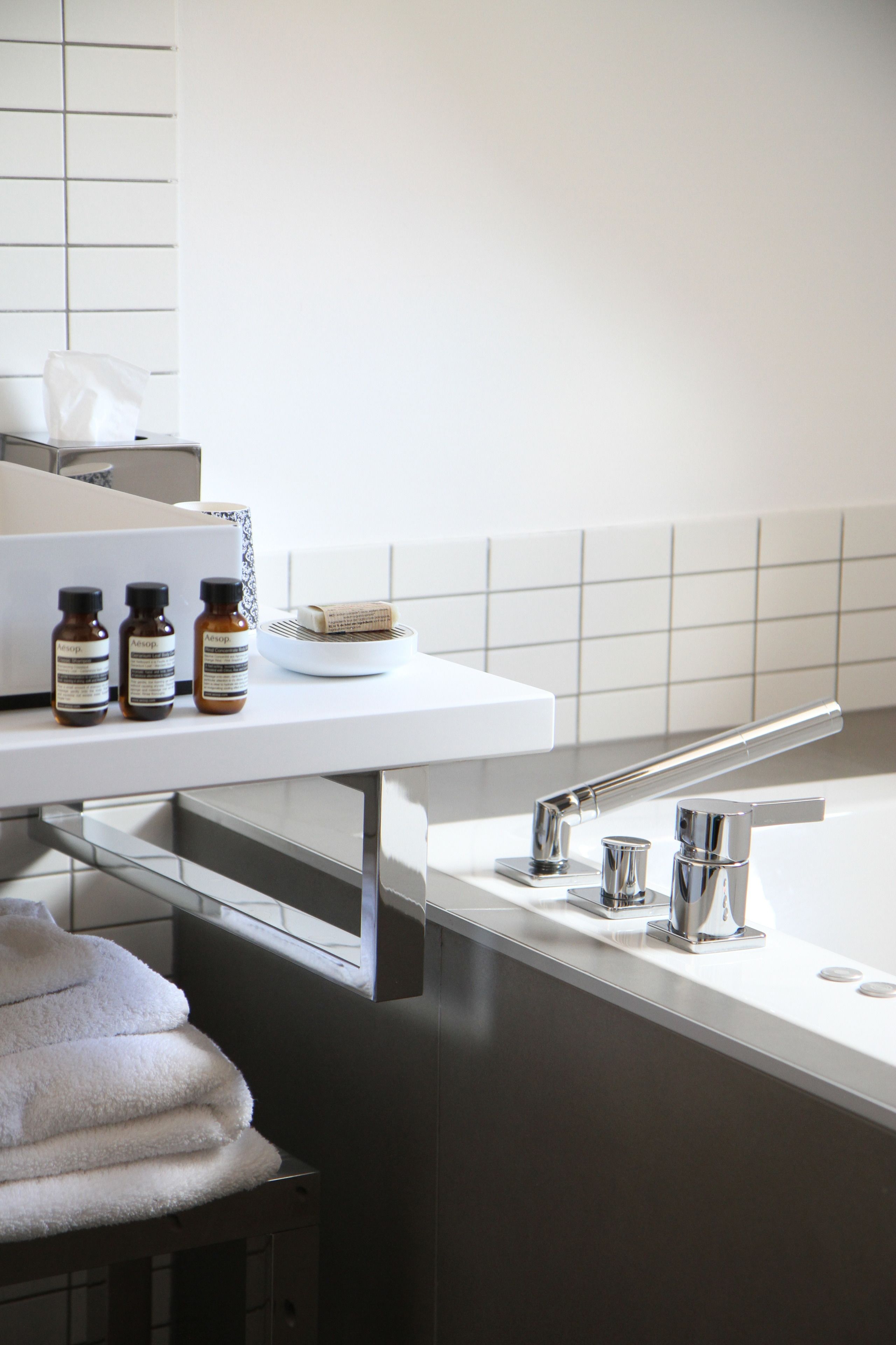 A bathroom with a white sink, a mirror, and a towel rack. There are three bottles on the counter.