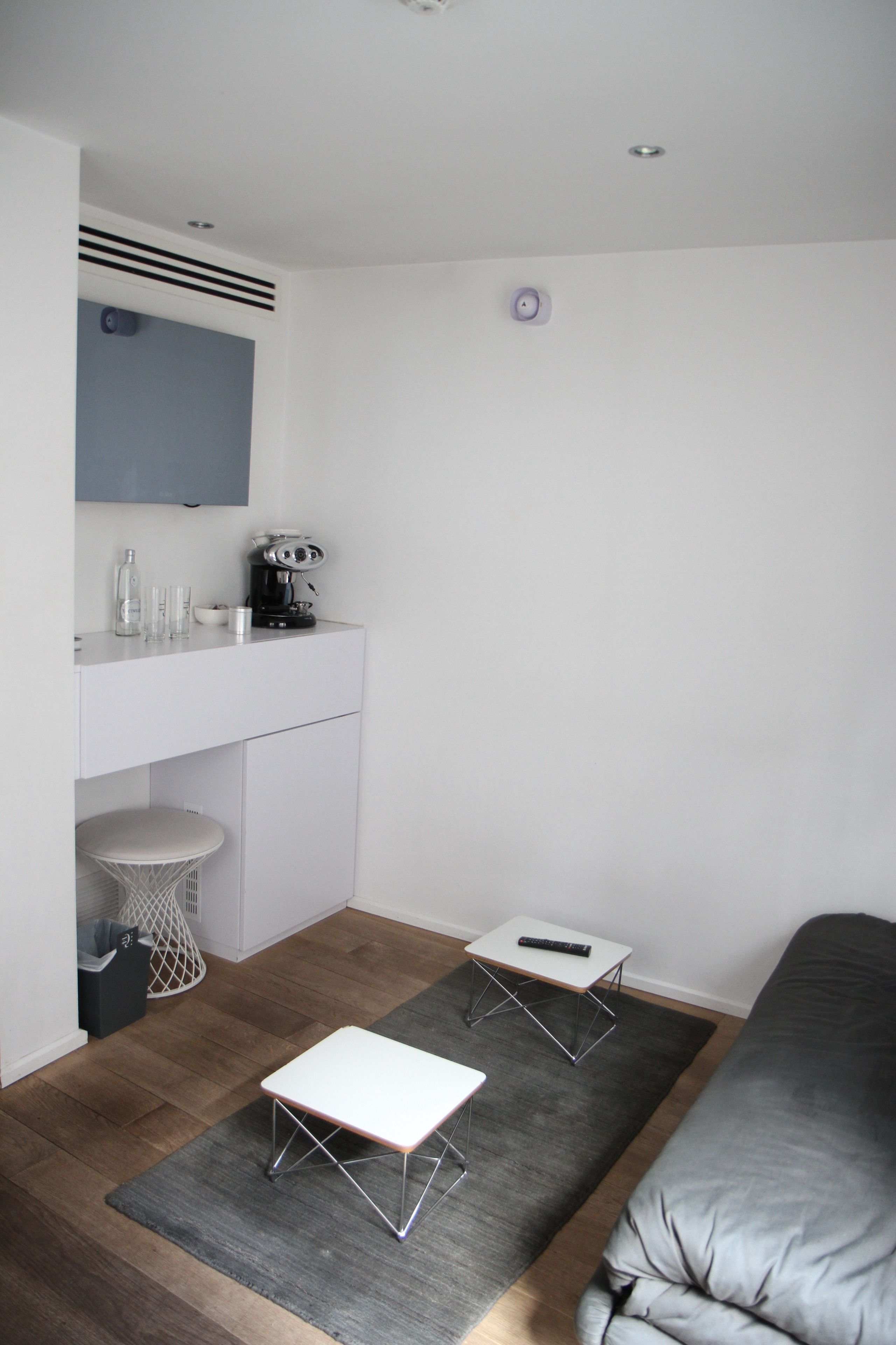 Een lichte, moderne kamer met een bed, een wit bureau, een stoel, een klein tafeltje en een afstandsbediening op de vloer.