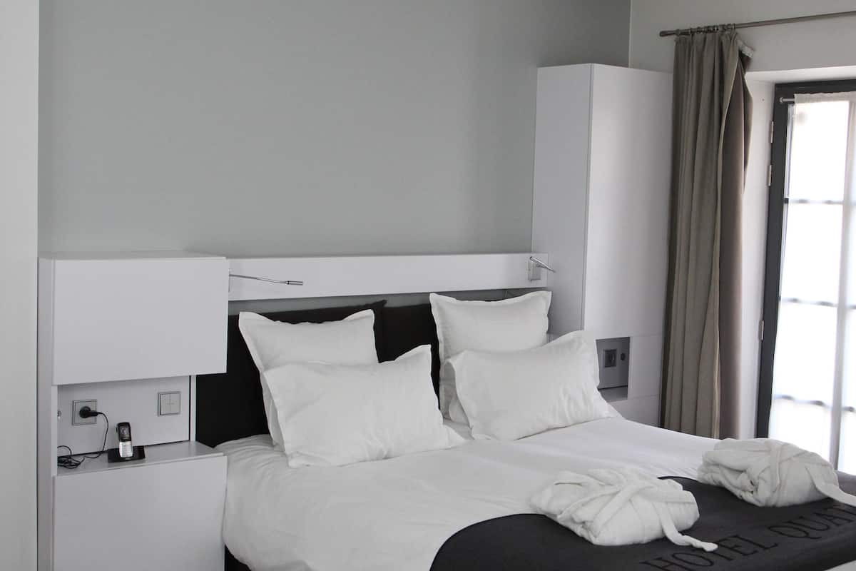 A modern hotel room with a large bed, a bedside table, a wardrobe, and a window with curtains.