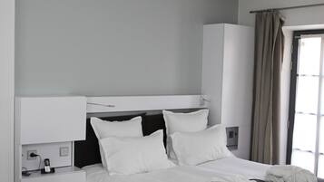 A modern hotel room with a large bed, a bedside table, a wardrobe, and a window with curtains.