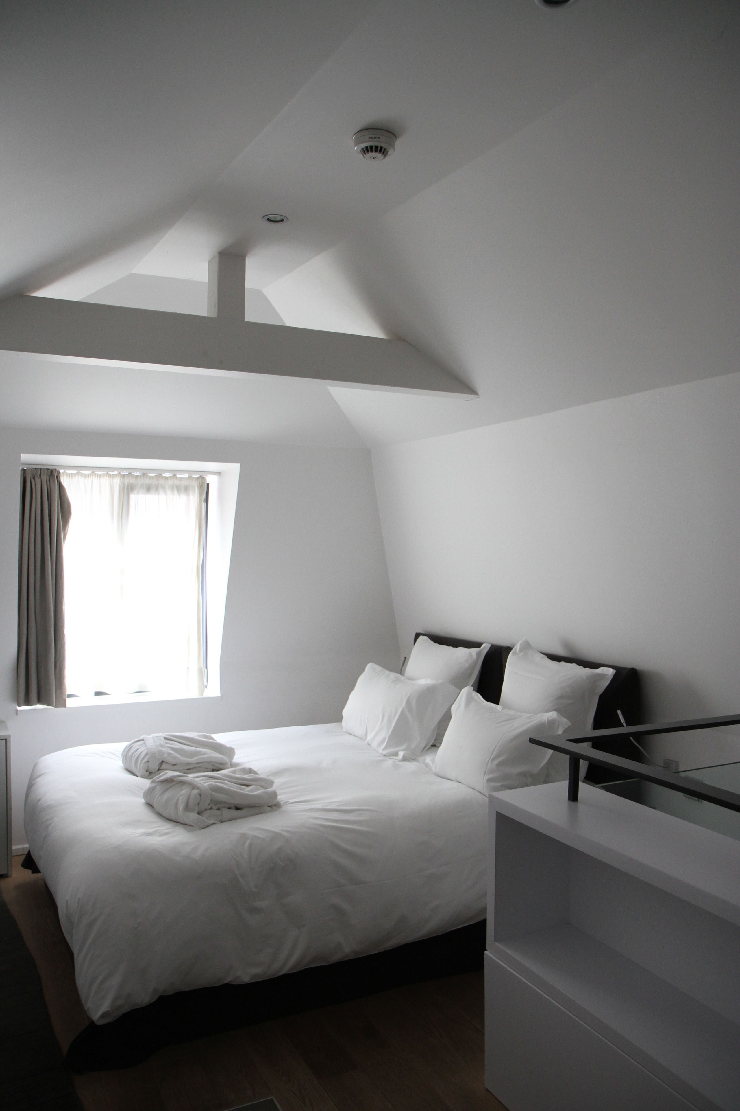 Un dormitorio con cama, ventana con cortinas, lámpara de techo y estante empotrado.