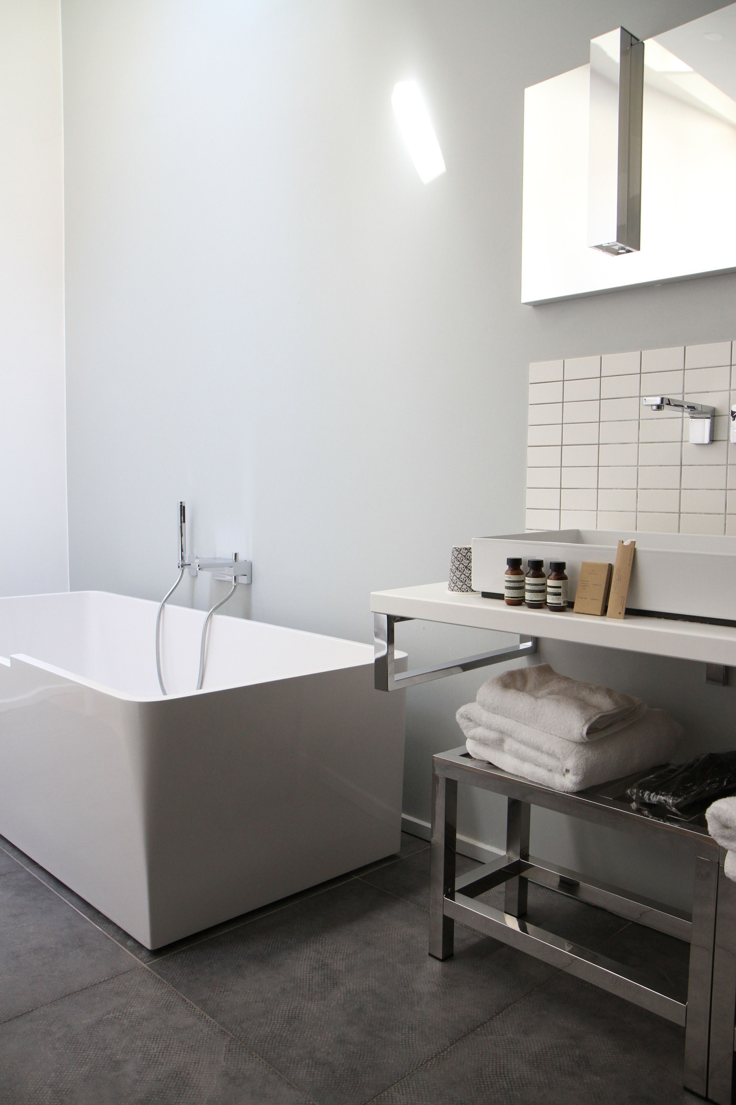 A modern bathroom with a freestanding bathtub, a vanity with a mirror, and a shelf with toiletries.