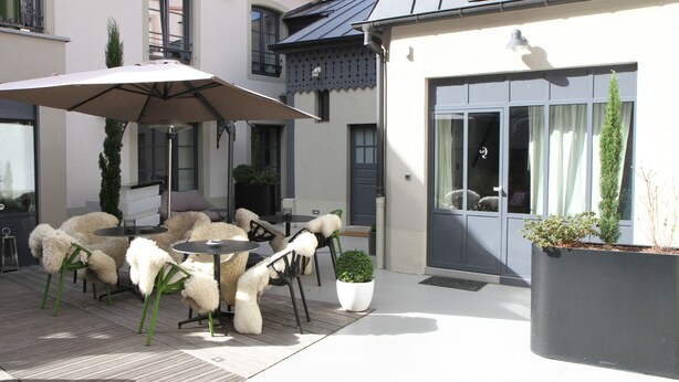An outdoor patio with round tables and chairs, a large umbrella, and potted plants. - Hôtel Quatorze (Colmar)