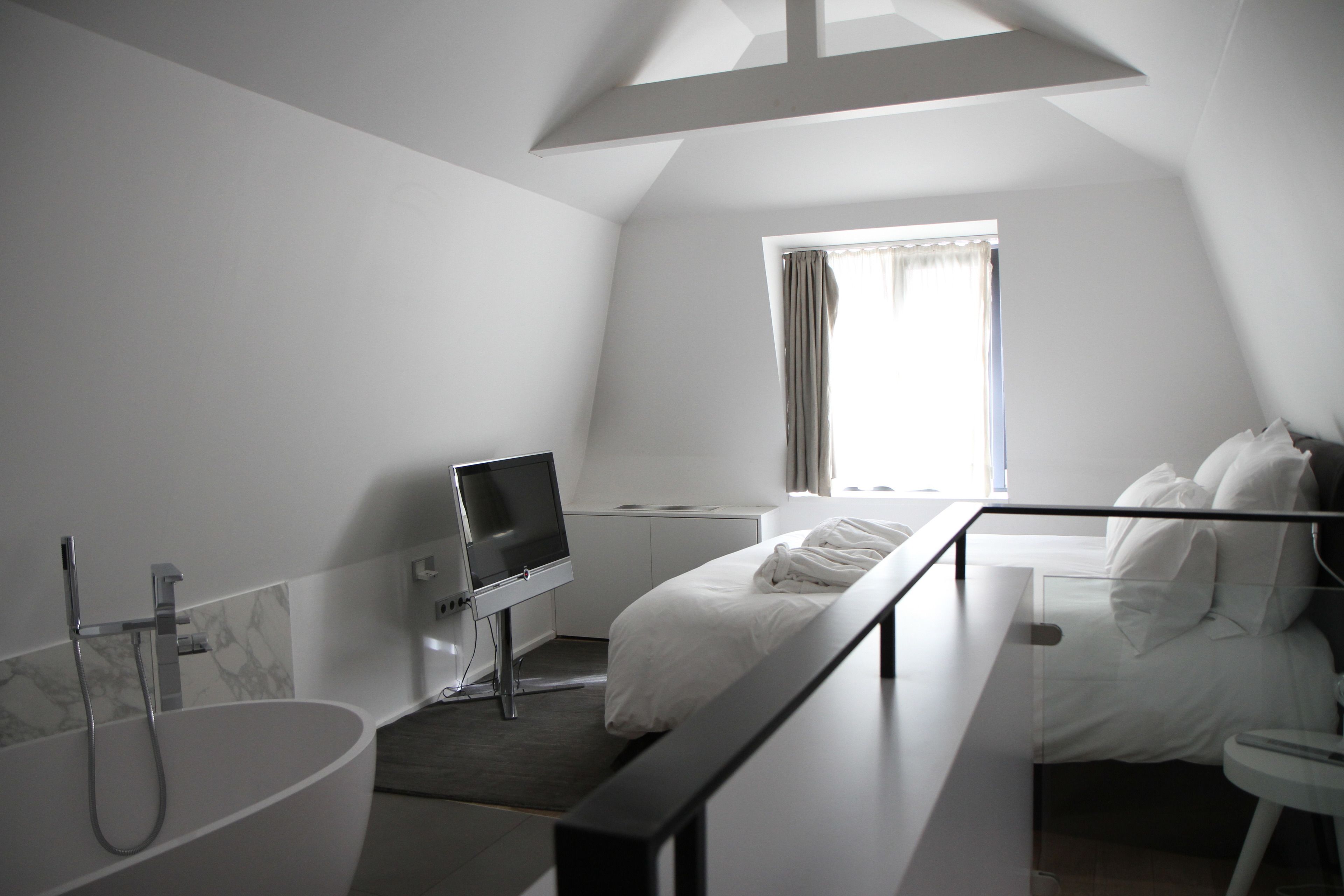 Ett modernt hotellrum med ett stort fönster, en platt-TV, ett badkar och en säng med vita sängkläder.