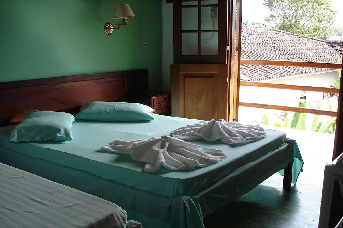 A room with two beds, a wooden headboard, a small cabinet, and a window with a view of a building.