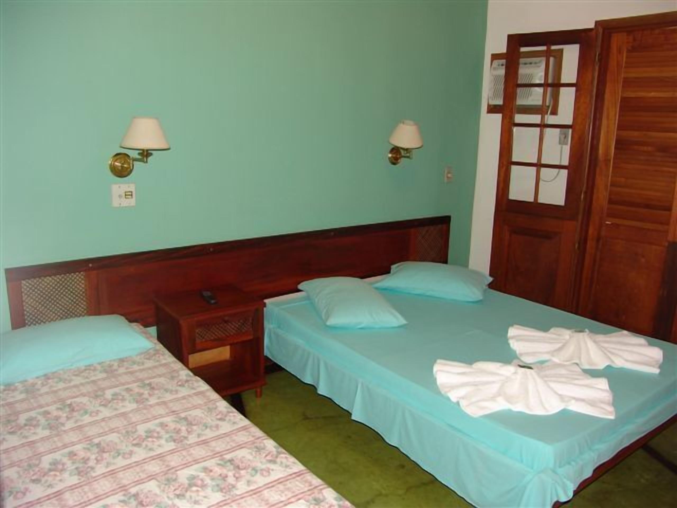 A room with two beds, a wooden headboard, a nightstand, and two wall-mounted lamps.