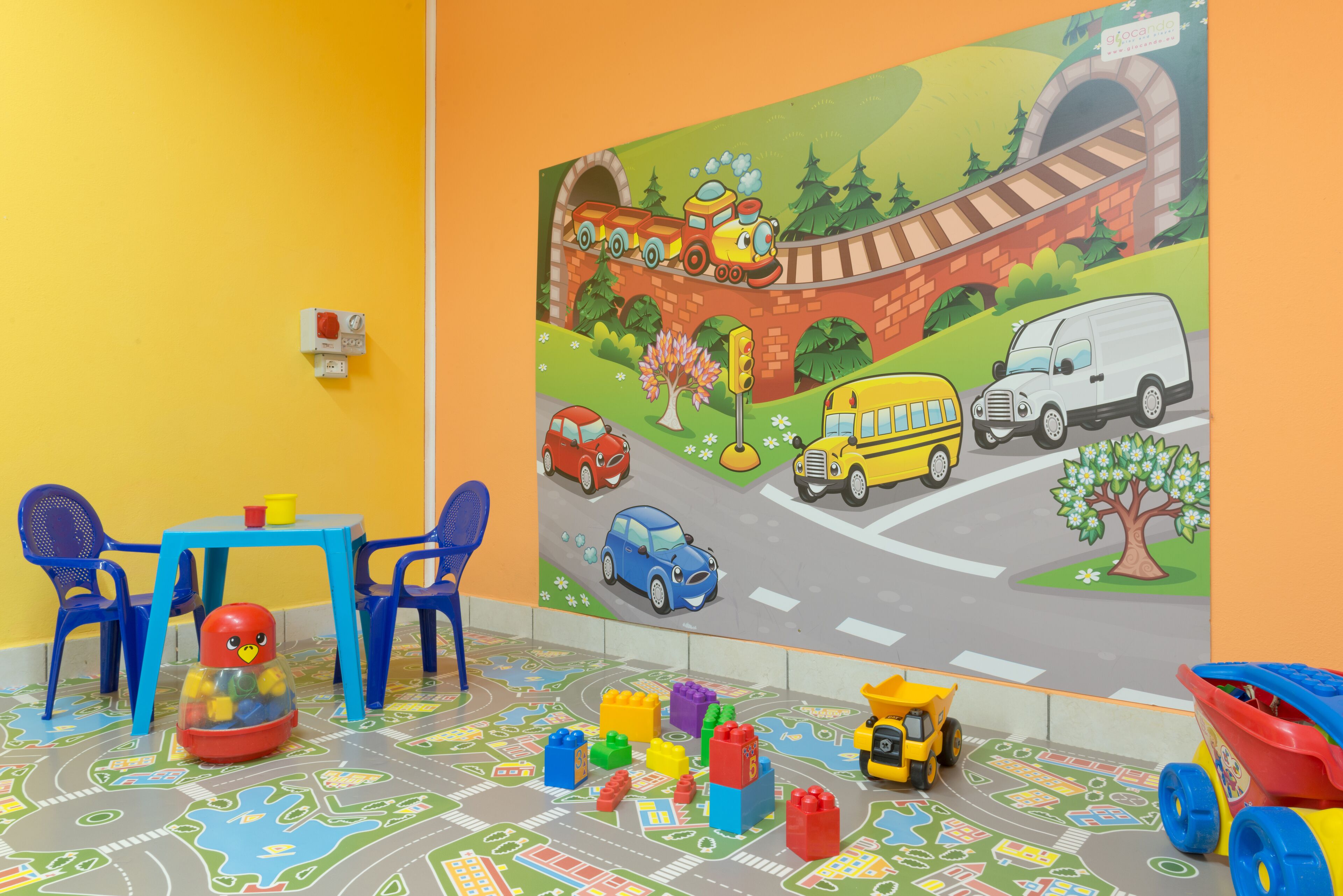 A children's playroom with a colorful mural, play mats, and toys.