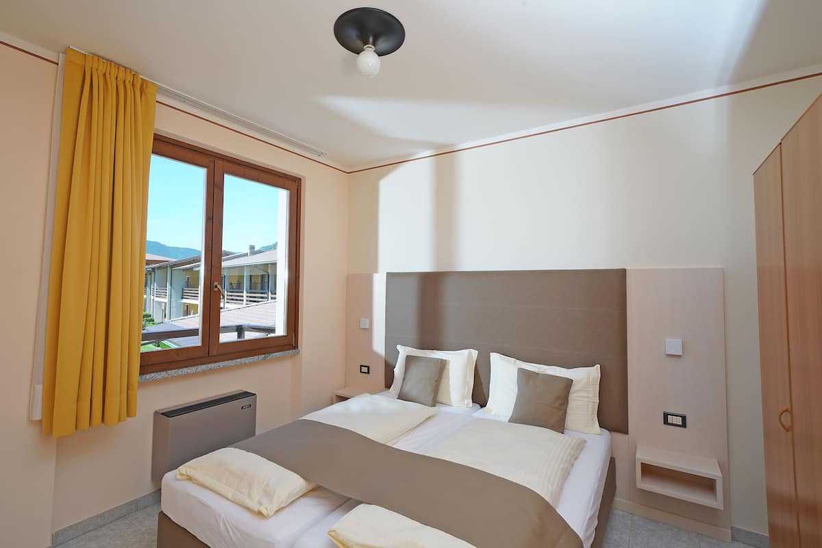 Een moderne hotelkamer met een groot bed, een nachtkastje, een raam met gordijnen en uitzicht op gebouwen.