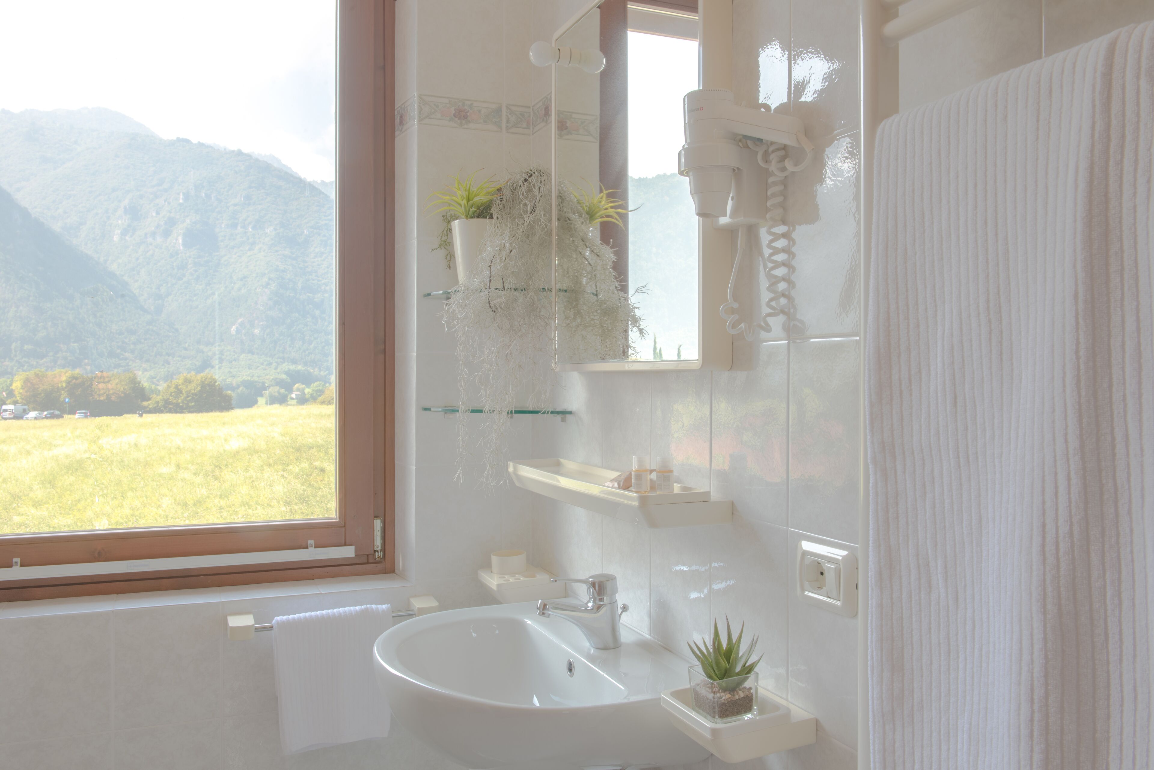 Een badkamer met een groot raam, een wastafel, een spiegel, een haardroger en een handdoekhouder.