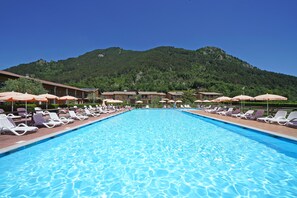 A swimming pool with lounge chairs and umbrellas, surrounded by buildings with a mountain in the background.