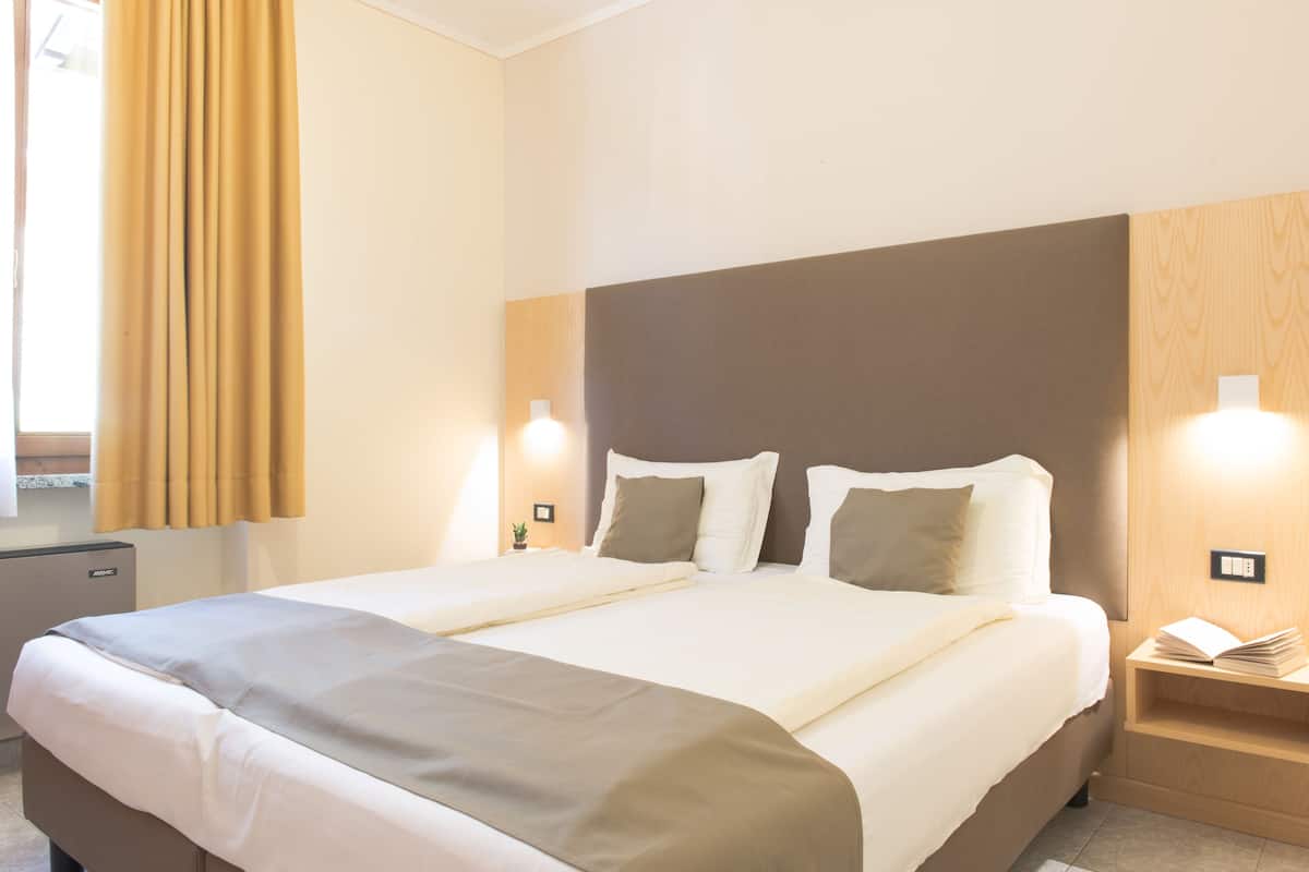 Een hotelkamer met een groot bed, een nachtkastje met een lamp en een houten hoofdeinde.