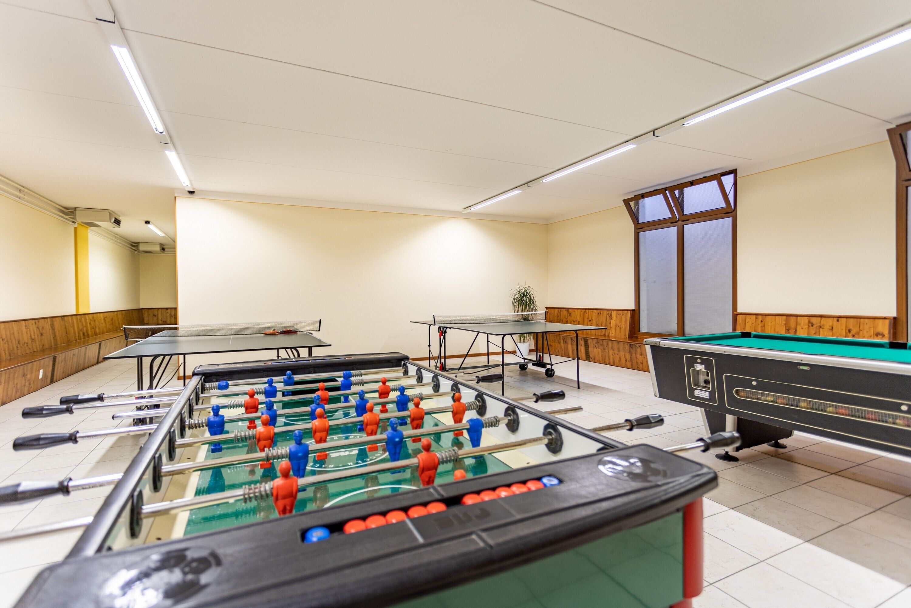 A room with multiple foosball tables, a pool table, and a ping pong table.