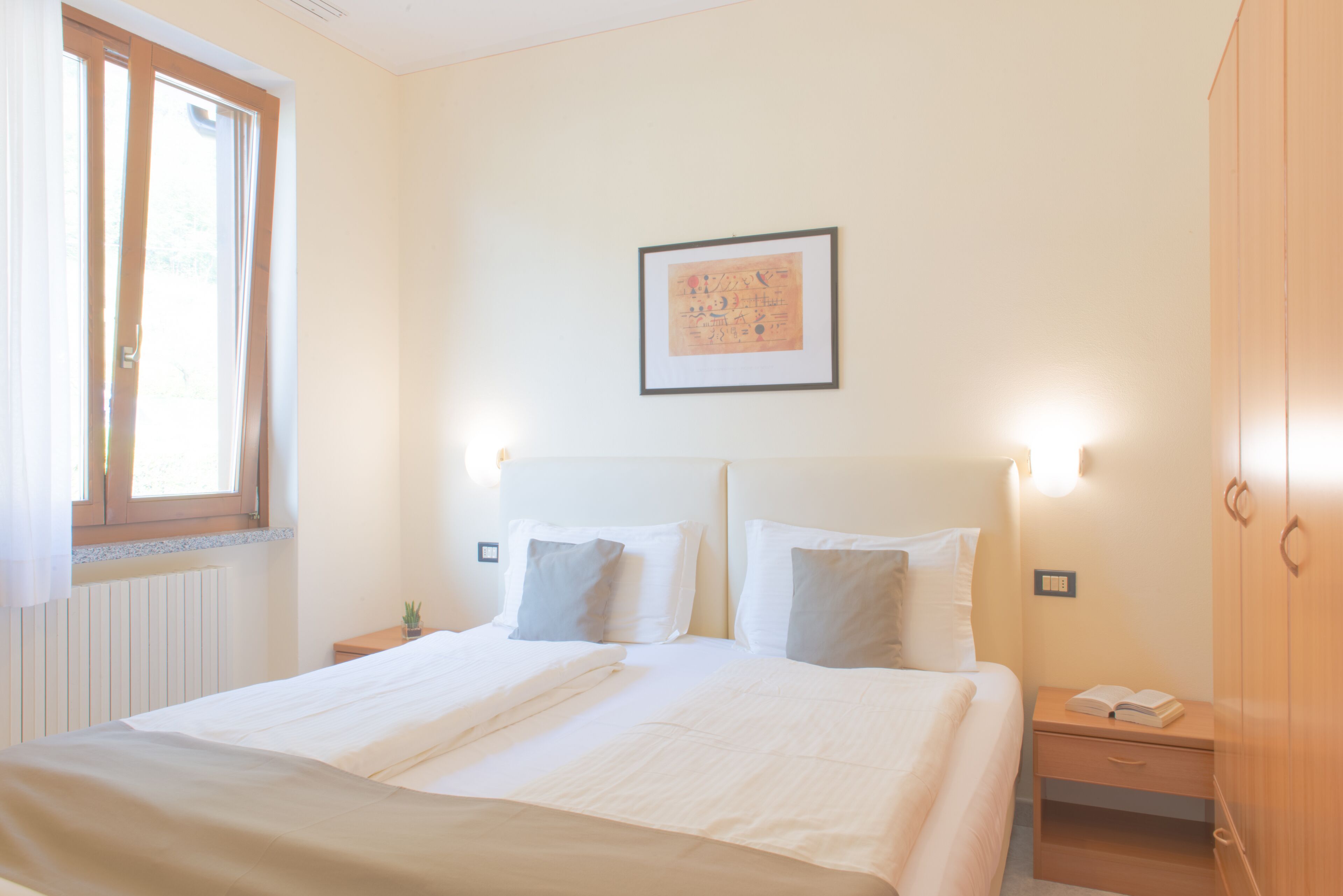 Habitación de hotel con una cama grande, mesitas de noche, un armario y un cuadro en la pared.