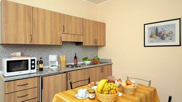 Una cocina con armarios de madera, microondas, cafetera y una mesa de comedor con mantel amarillo.
