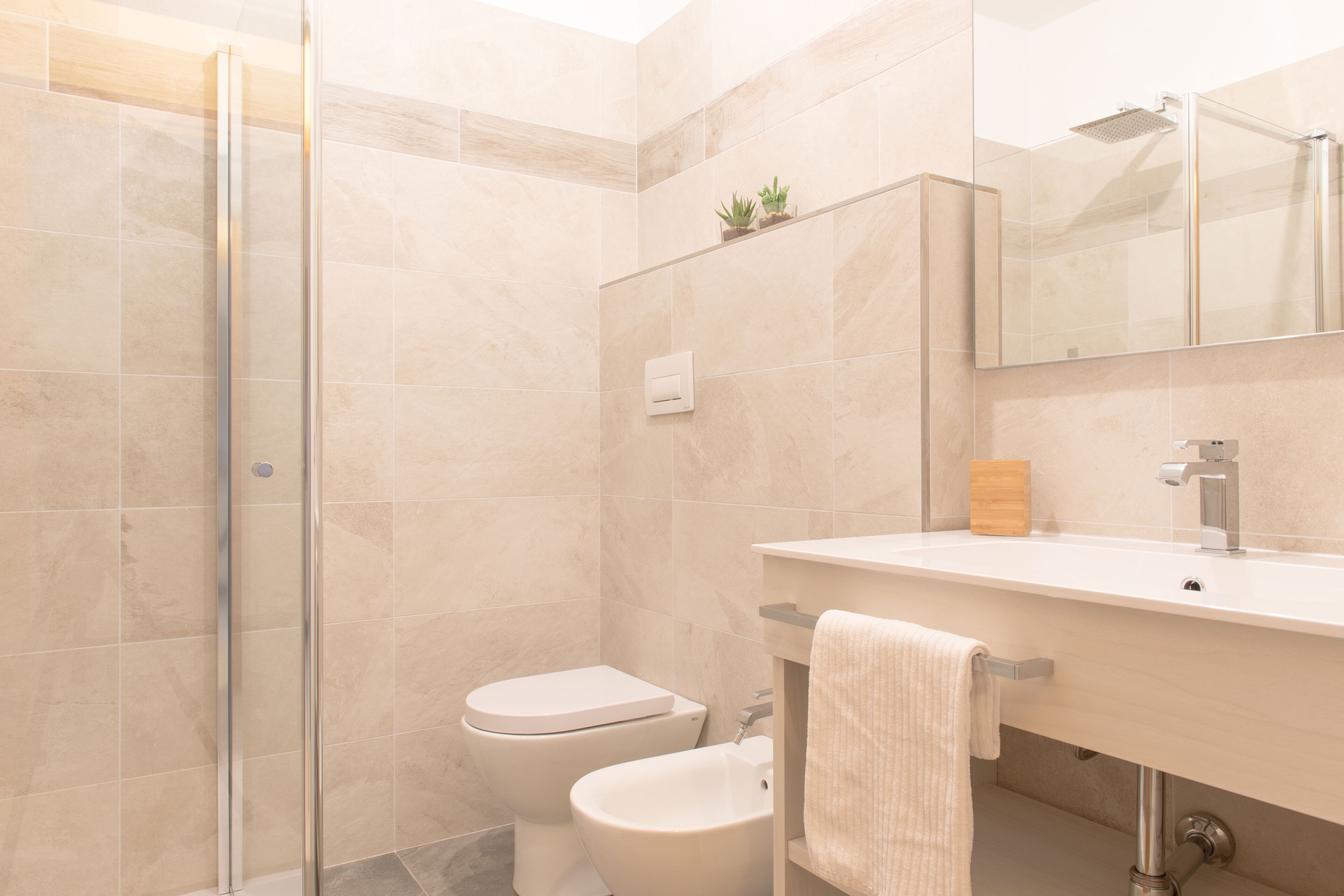 A modern bathroom with a glass shower enclosure, a toilet, a bidet, and a sink with a mirror above.