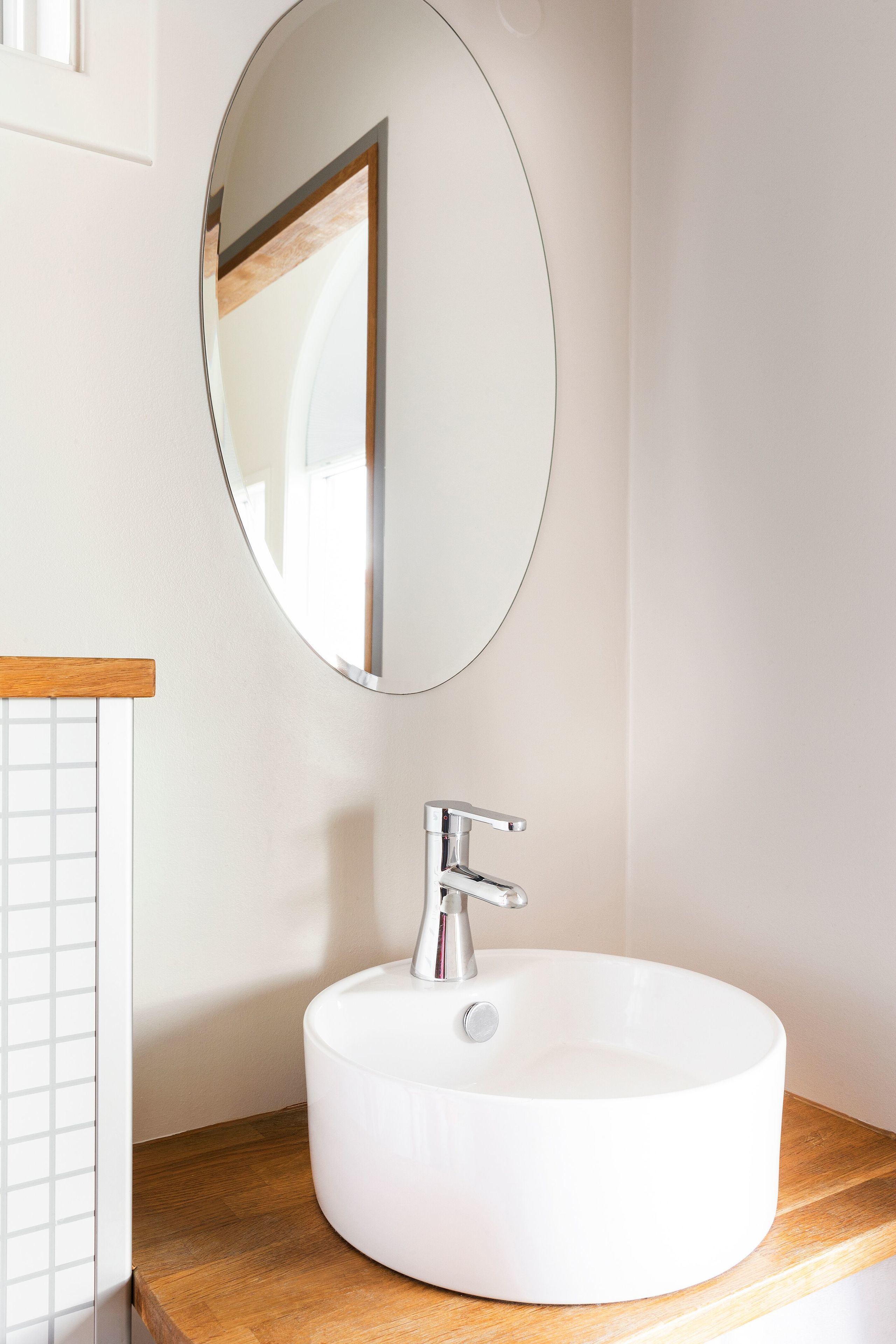 Un baño con un lavabo blanco, un espejo redondo y una encimera de madera.