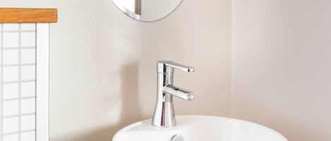 A bathroom with a white sink, a round mirror, and a wooden countertop.