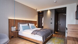 A modern bedroom with a wooden bed, bedside tables, a chair, and a walk-in closet. - Hótel Berg (Reykjanesbær)