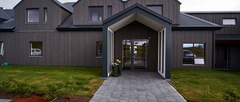 A modern building with a symmetrical facade, a central entrance with a covered walkway, and a well-maintained lawn.