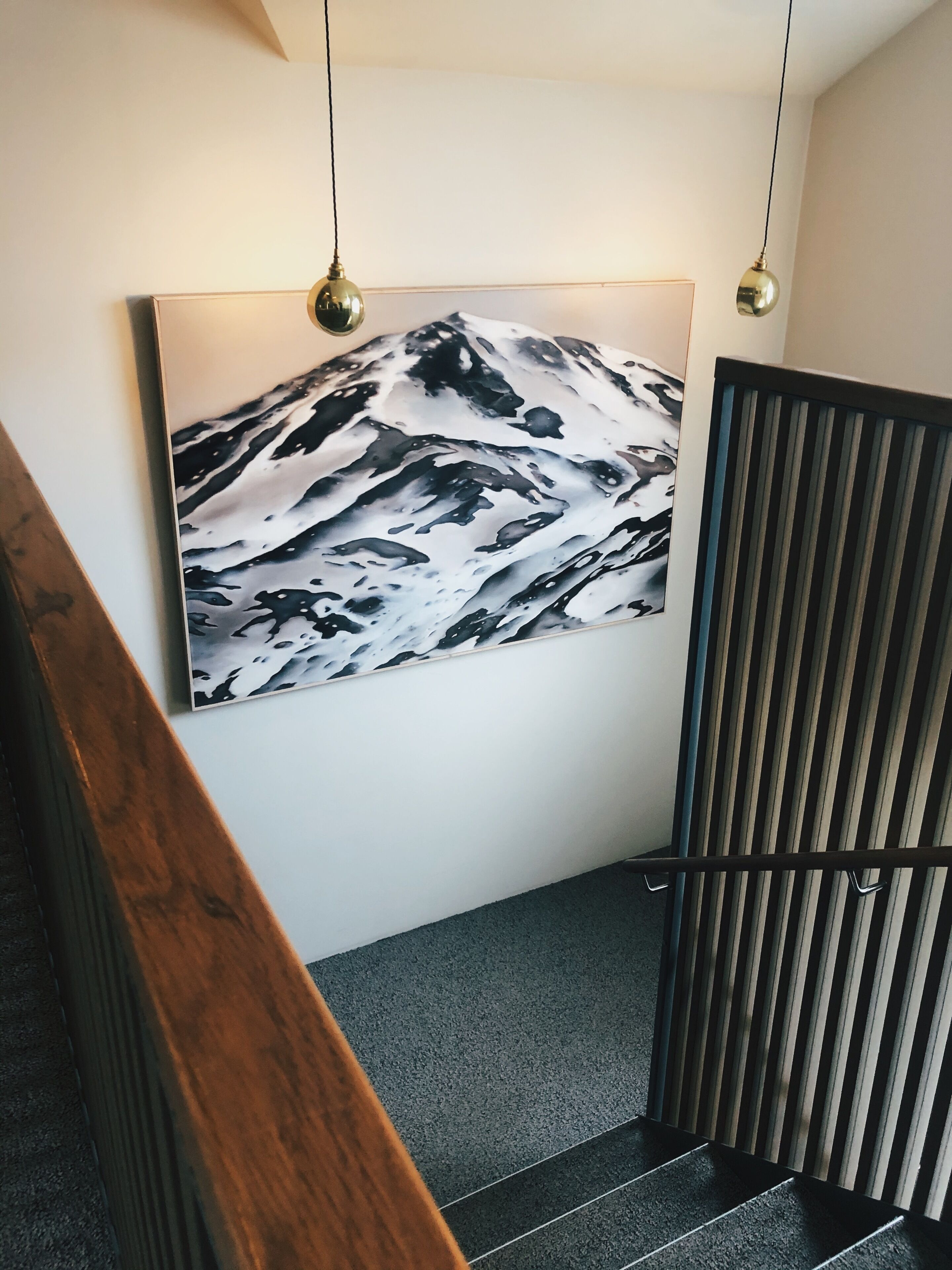 A staircase with a wooden handrail, a black and white abstract painting on the wall, and a black metal partition.