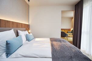Habitación de hotel con una cama grande, cabecera y vista al comedor a través de un acceso.