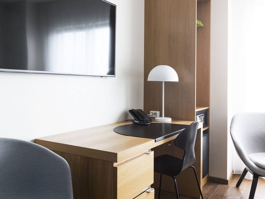 Ein moderner Arbeitsraum mit einem Holztisch, zwei Stühlen, einem Flachbildfernseher, einer Lampe und einer eingebauten Regaleinheit.