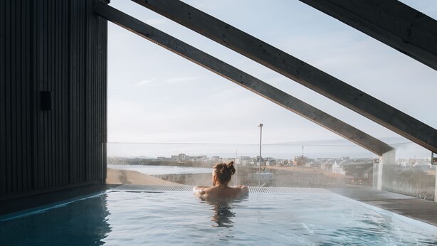 A person in a swimming pool with a view of a cityscape and a bridge in the background. - Hótel Berg (Reykjanesbær)