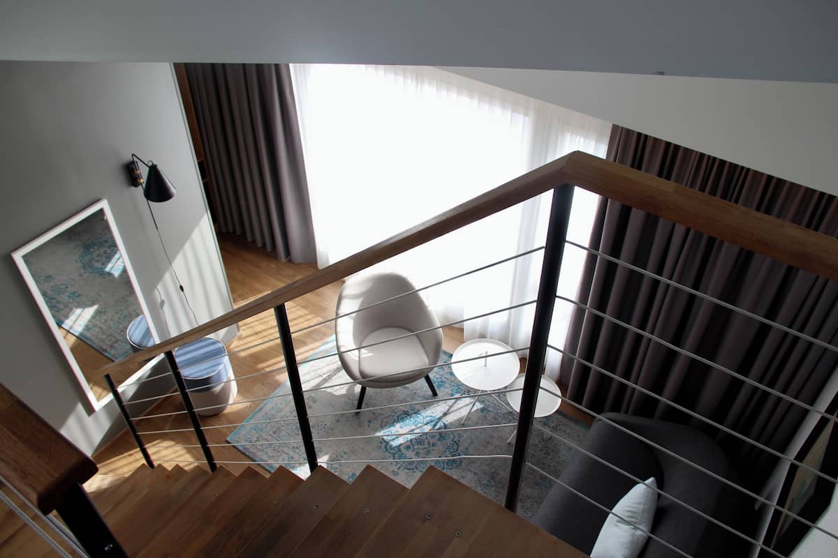 A modern interior with a wooden staircase, a white armchair, a small round table, and a patterned rug.