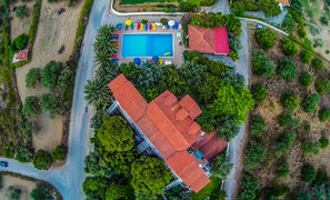 An aerial view of a property with a swimming pool, a red-roofed building, and lush greenery. - Barbara Studios & Apartments (Kefalonia)