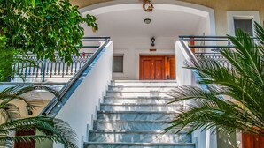 Una imponente escalera conduce a un balcón con barandillas ornamentales, rodeado de exuberante vegetación.