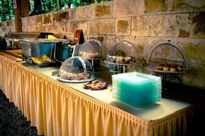 A buffet setup with covered food stations, a stack of blue plates, and a stone wall background.