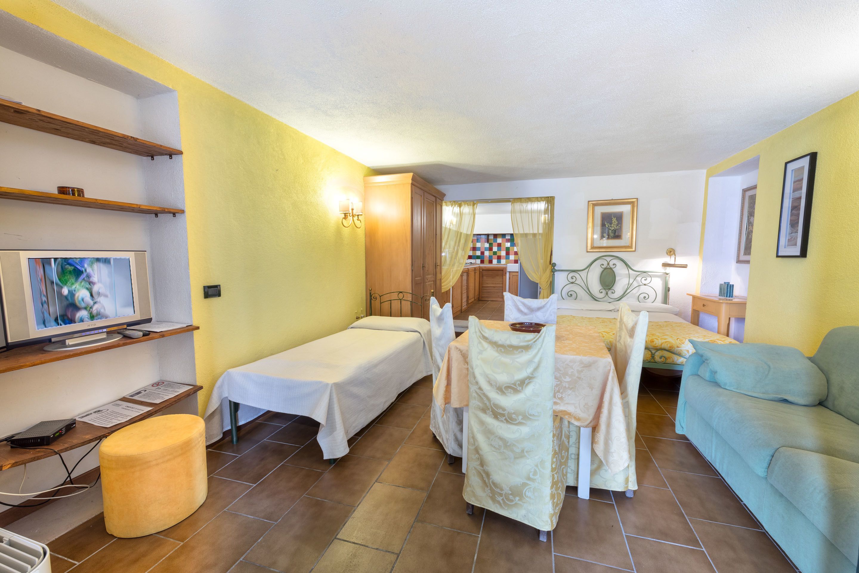 A room with two single beds, a sofa, a TV, a small table, and a chair.