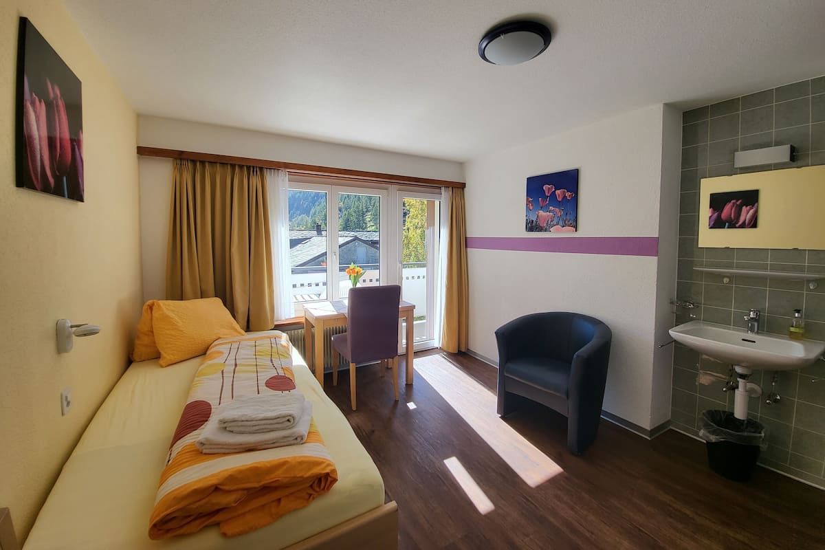 A hotel room with a bed, a desk, a chair, a bathroom with a sink, and a view of the outside.