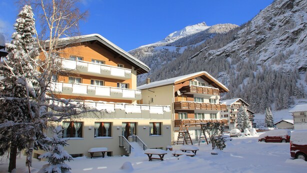 A snow-covered building with multiple balconies and a ski lift visible in the background. - Pension Heino (Saas Grund)