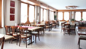 A spacious dining area with wooden tables and chairs, large windows, and a high ceiling with exposed beams. - Pension Heino (Saas Grund)