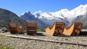 Three wooden chairs with a unique design, positioned on a rocky surface with a mountainous backdrop. - Pension Heino (Saas Grund)