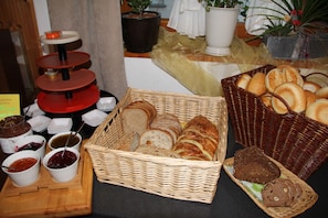 A buffet table with various breads, jams, and a tiered condiment dispenser. - Pension Heino (Saas Grund)