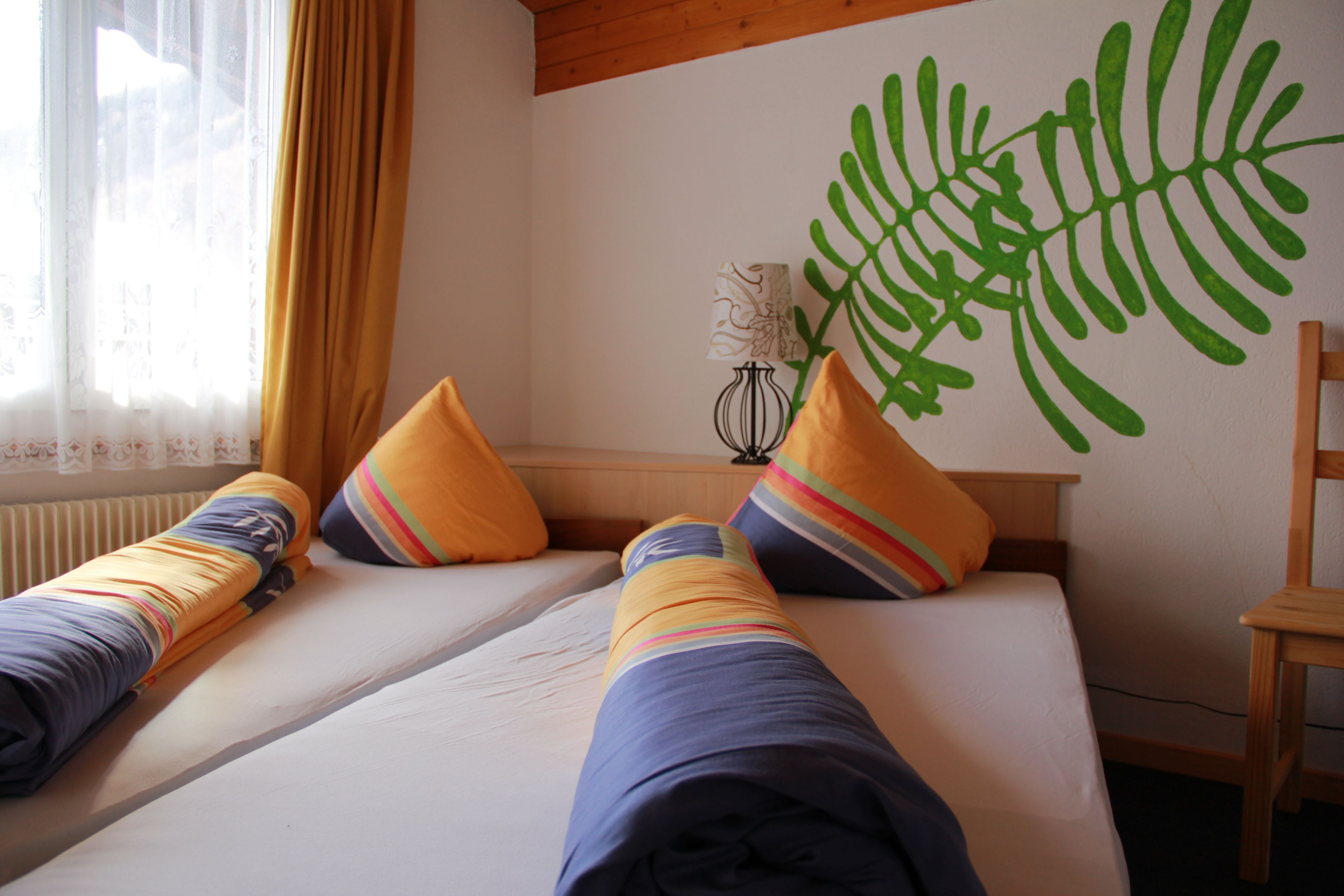 A room with two beds, each with a rolled-up blanket and a pillow with a striped pattern.