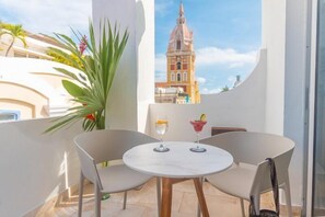 A balcony with two chairs and a table, two drinks, a potted plant, and a view of a historic building. - Delirio (Cartagena)