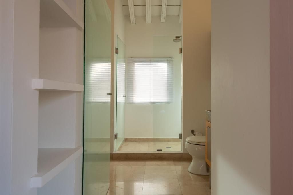 A bathroom with a glass shower enclosure, a toilet, and a window with blinds.