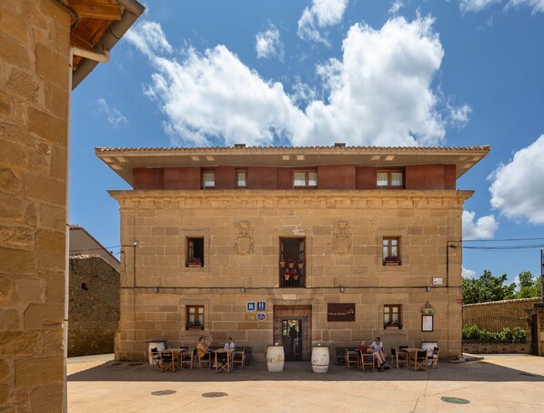 A stone building with a tiled roof, multiple windows, and outdoor seating area with tables and chairs. - Villa de Abalos (Abalos)