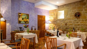 A dining area with tables set for a meal, wooden chairs, and a stone wall.