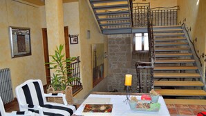 A cozy room with a wooden staircase, a black and white striped chair, a table with books and a candle, and a stone wall.