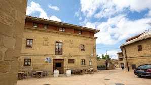 A courtyard with outdoor seating, stone buildings, and a car parked nearby.