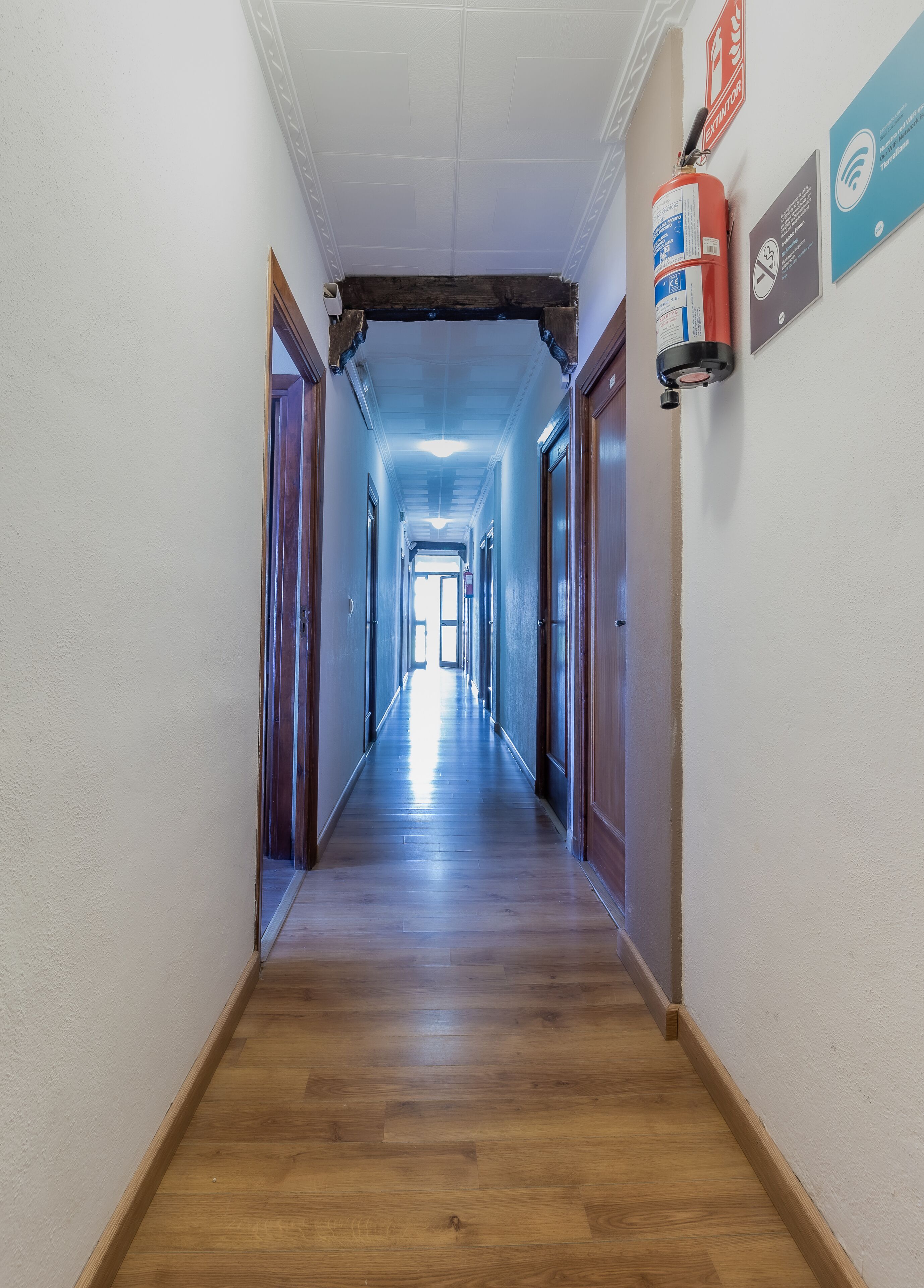Un largo pasillo estrecho con suelo de madera y paredes blancas.