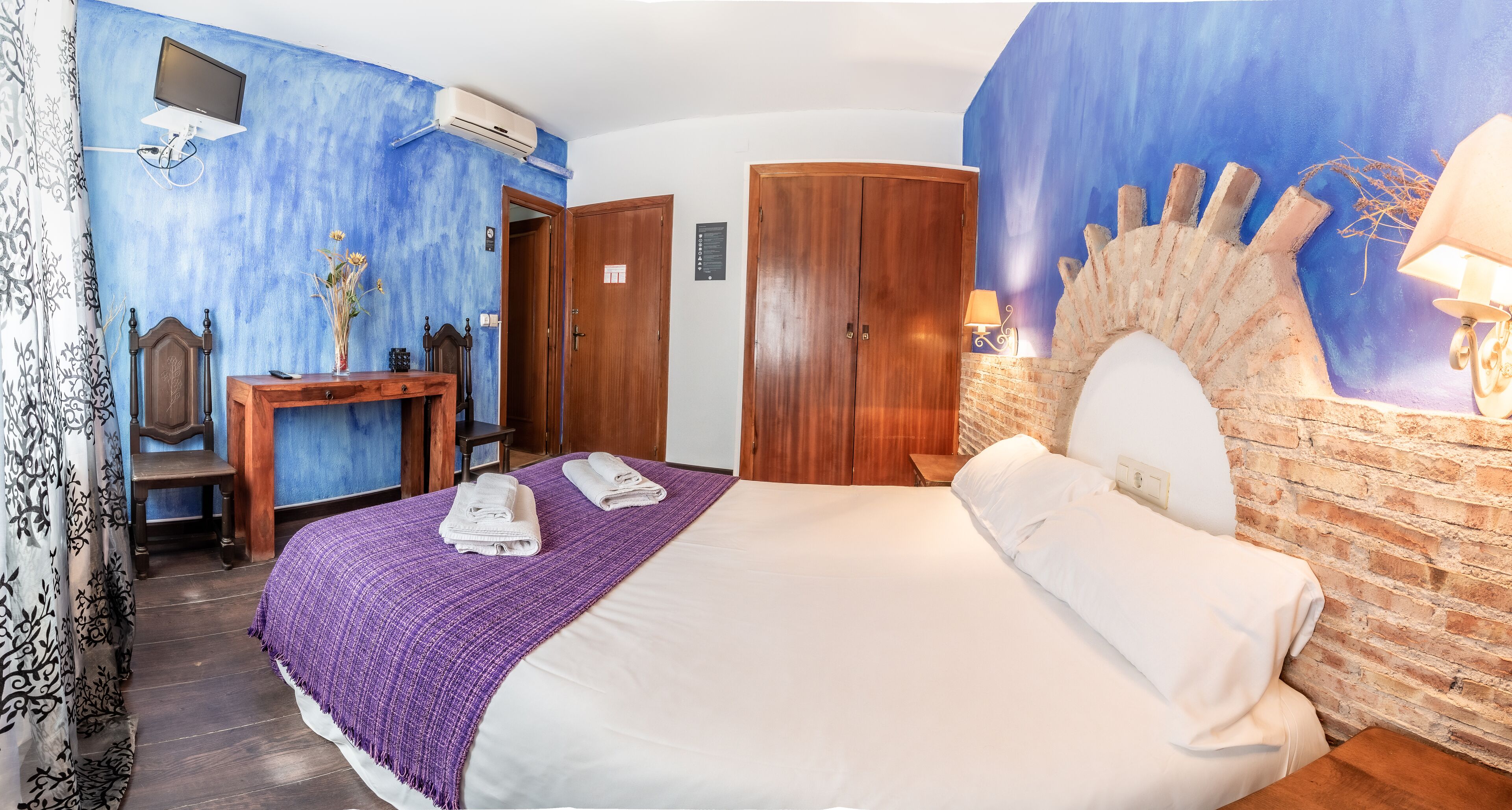 Habitación de hotel con cama, escritorio, silla, televisor y un mural en la pared.