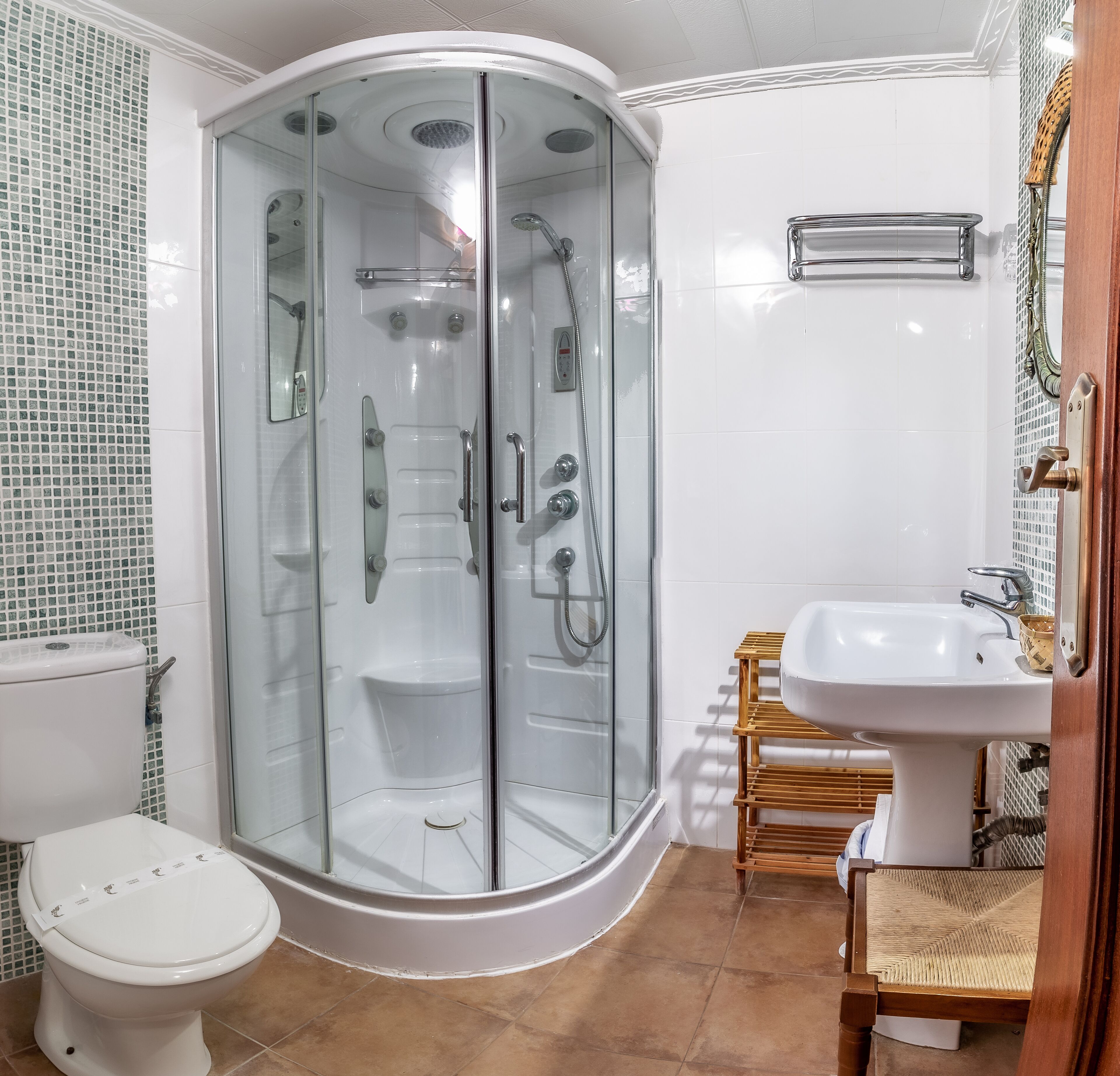 Uma casa de banho moderna com cabine de duche em vidro, sanita, lavatório e uma cadeira de madeira.