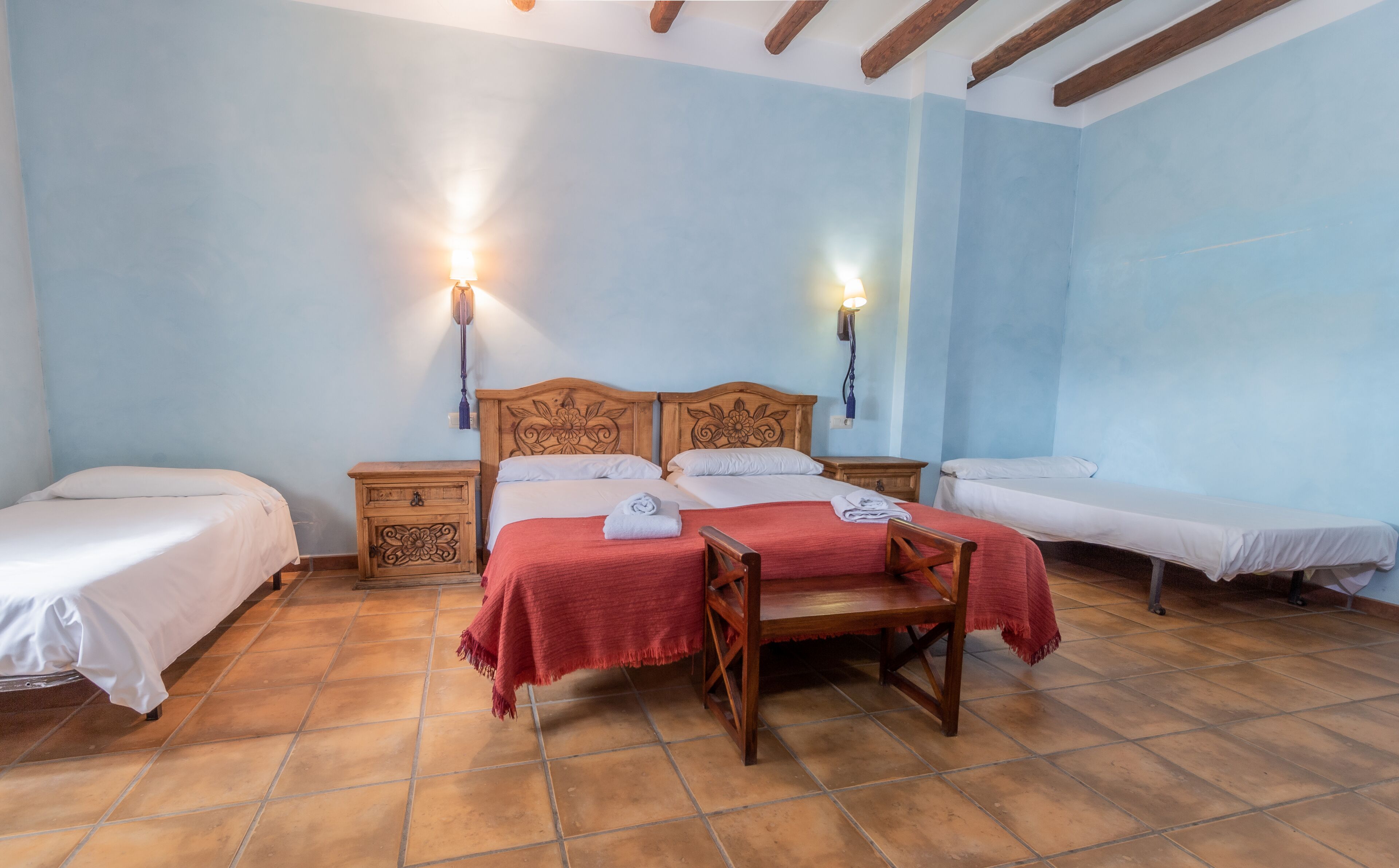 A bedroom with two beds, a wooden headboard, and a small wooden chair. There are two bedside tables with lamps.