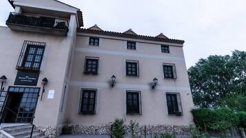Un edificio de varios pisos con fachada de piedra, múltiples ventanas con barrotes y un balcón en el piso superior.